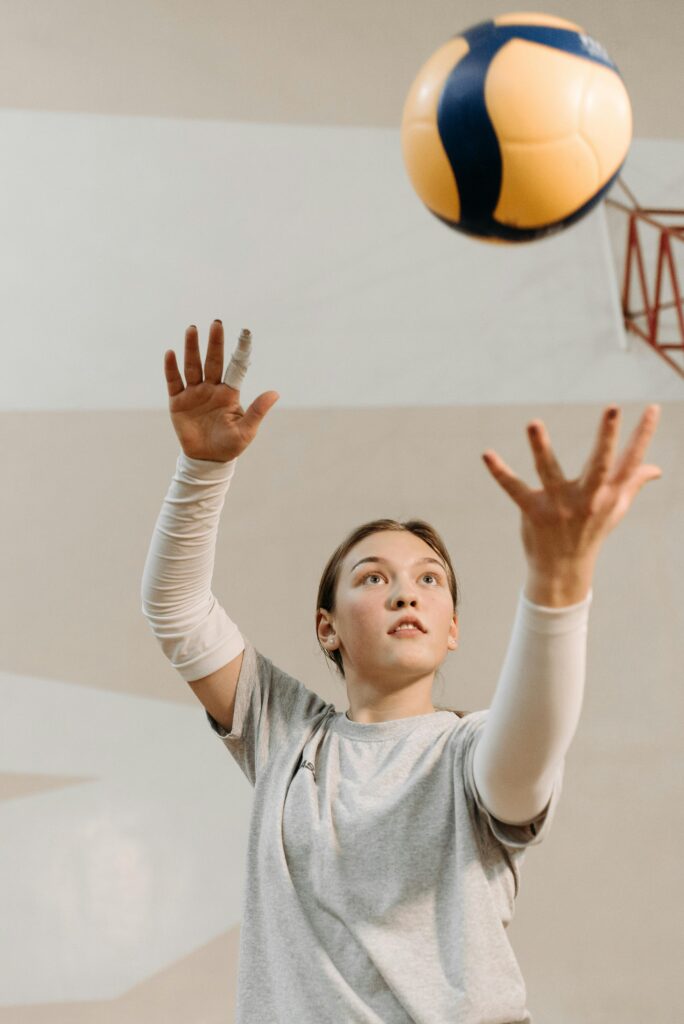 A determined female athlete reaches for a volleyball in an indoor practice setting.