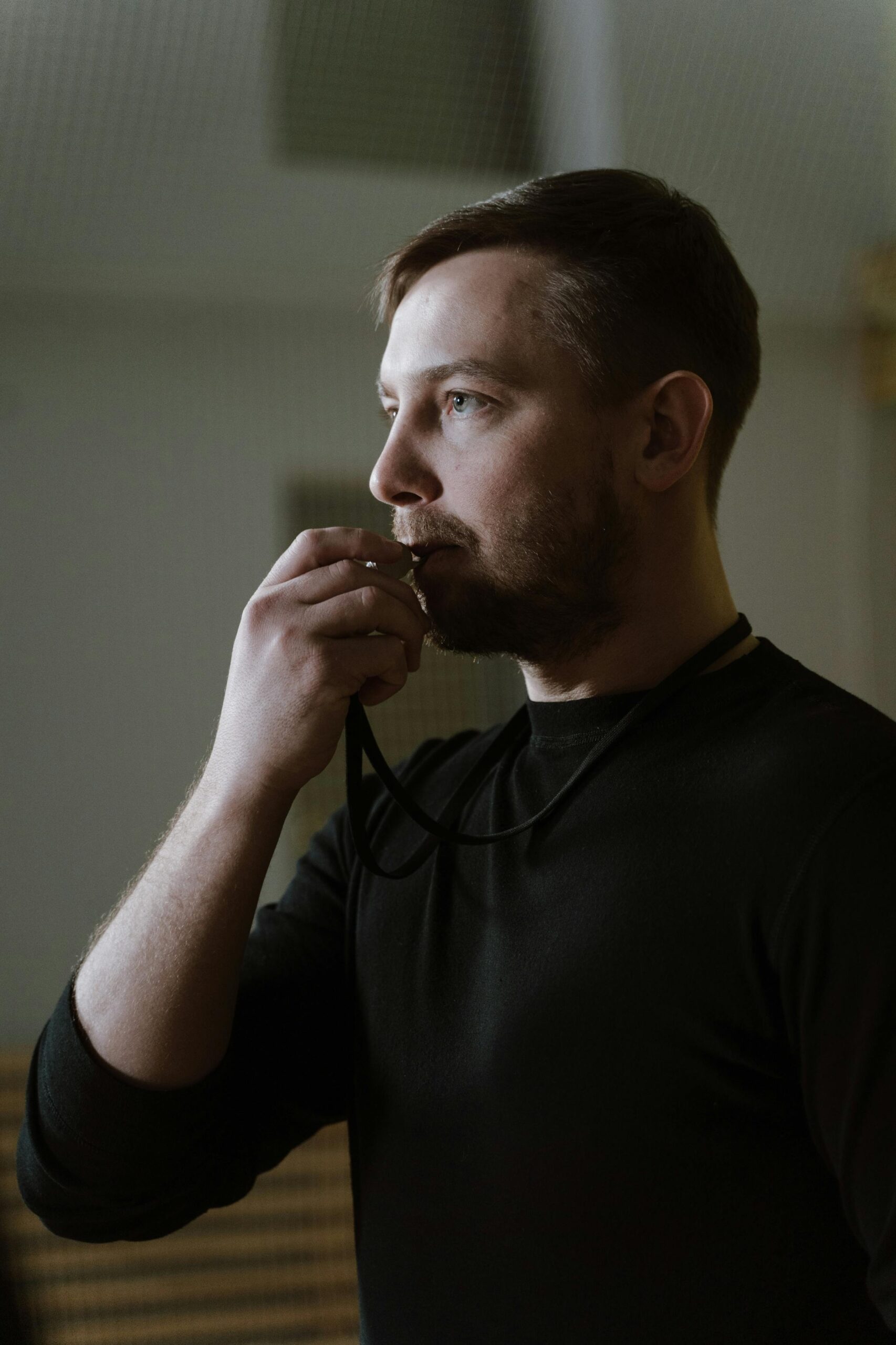 A focused sports coach in black attire holding a whistle, demonstrating leadership and determination indoors.